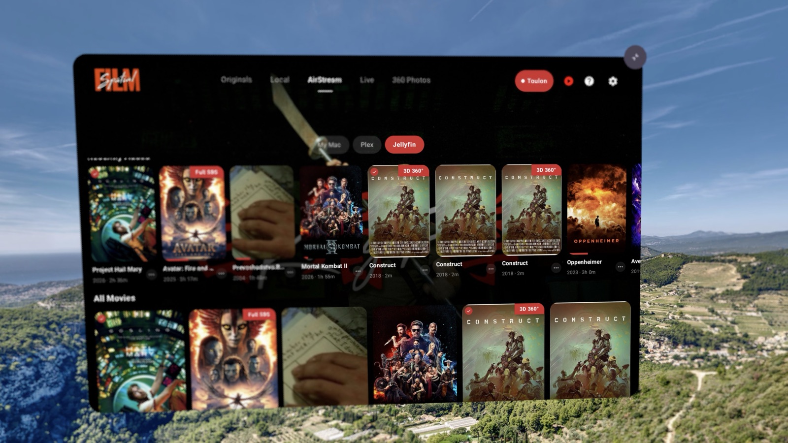 Spatial Film on Samsung Galaxy XR — a Jellyfin poster wall with Full SBS and 3D 360° badges on the cards, watched checkmarks, and runtimes, floating over a coastal hillside.