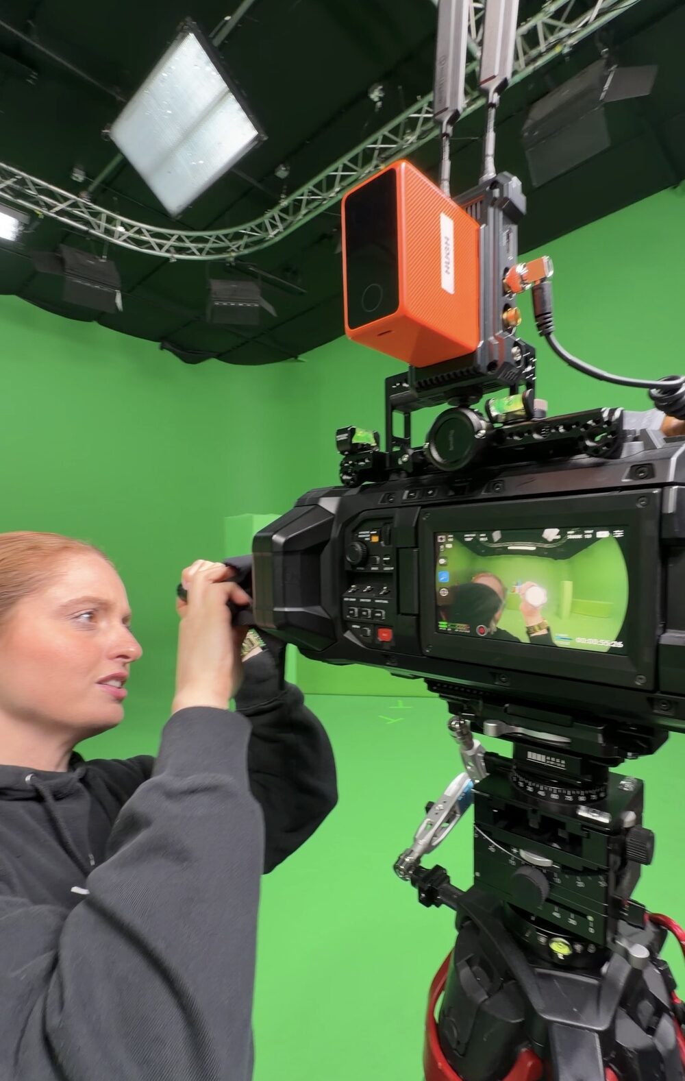 A camera operator lining up an URSA Cine Immersive with an NDI encoder mounted on top, on a green screen stage
